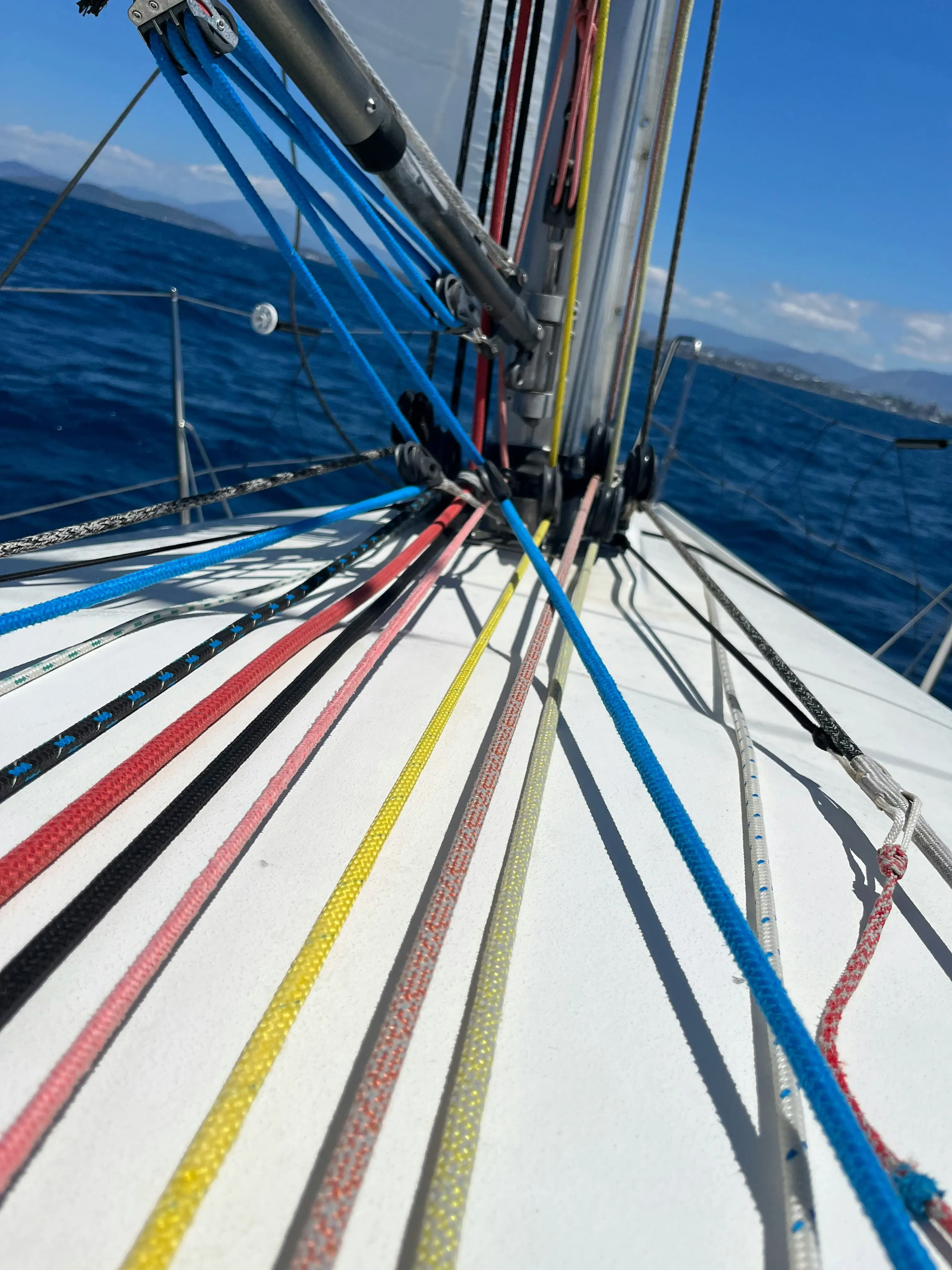 Close-up of colorful running rigging and halyards on a sailboat deck, with the mast and deep blue sea in the background.