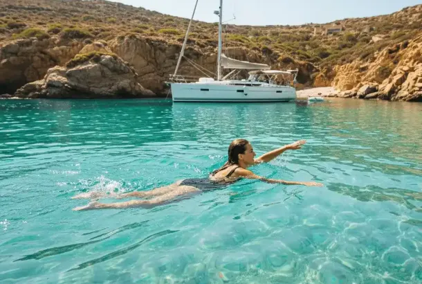 A person swimming in crystal clear turquoise waters off a beautiful, secluded cove, with a yacht visible in the background.