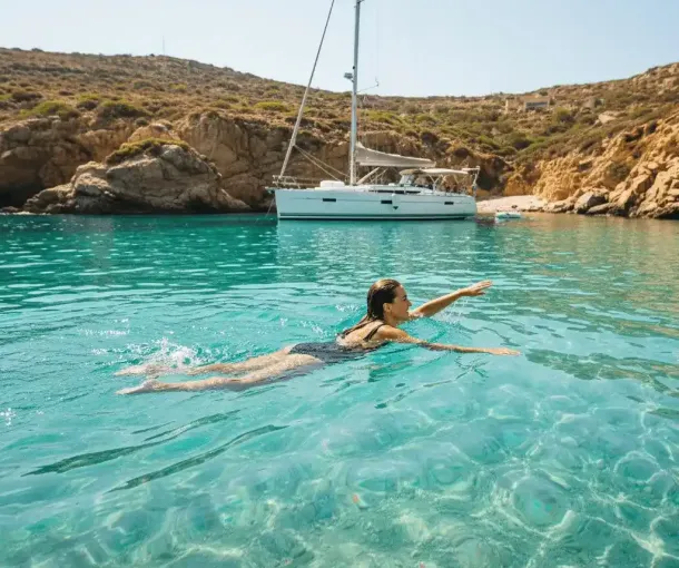 A person swimming in crystal clear turquoise waters off a beautiful, secluded cove, with a yacht visible in the background.