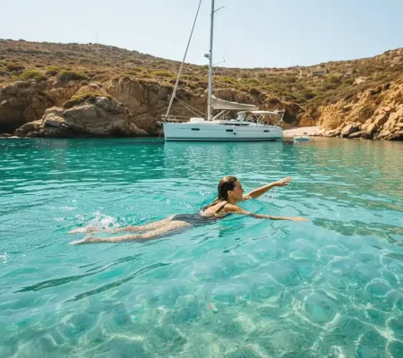 A person swimming in crystal clear turquoise waters off a beautiful, secluded cove, with a yacht visible in the background.
